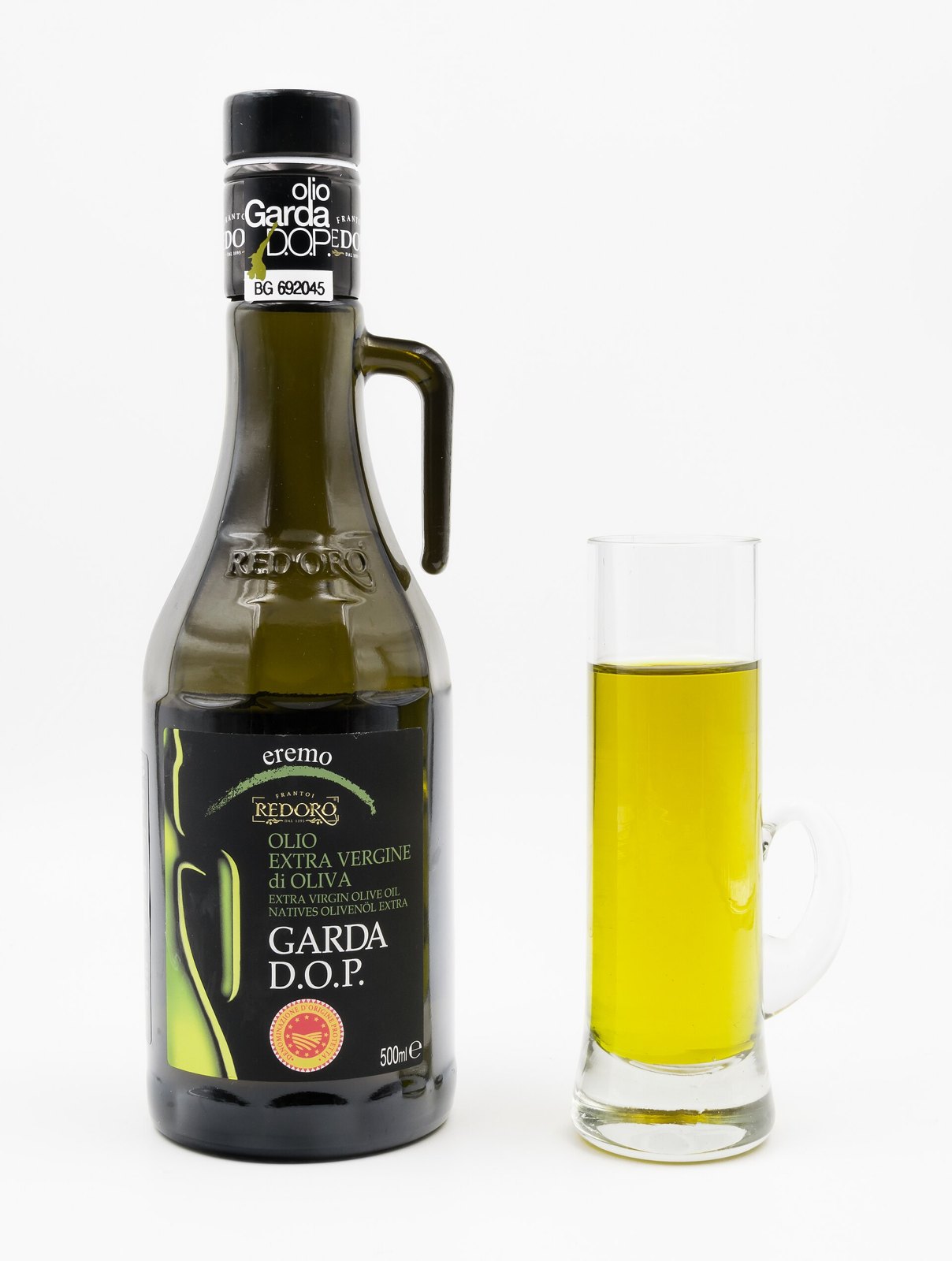 A dark green bottle of extra virgin olive oil beside a small glass filled with the oil, clear and bright golden-green