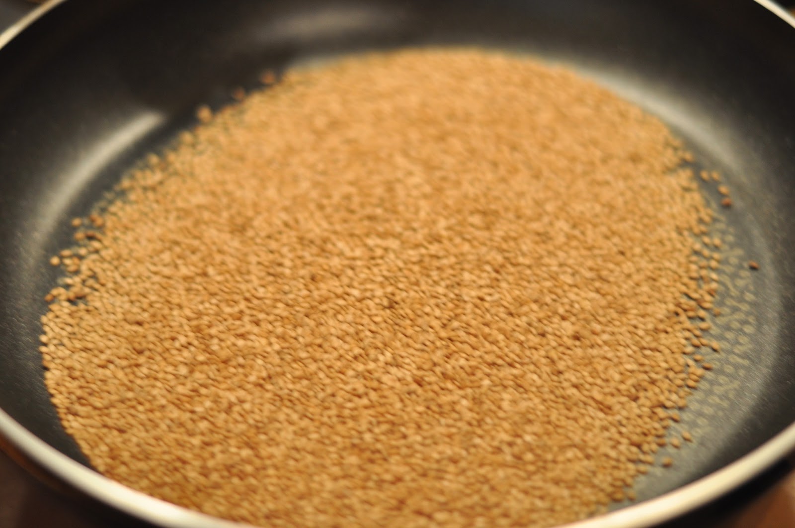 Sesame seeds being roasted and stirred in a wide pan